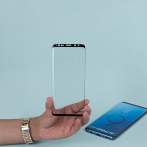 Close-up of a hand holding a transparent phone screen protector against a blue background.